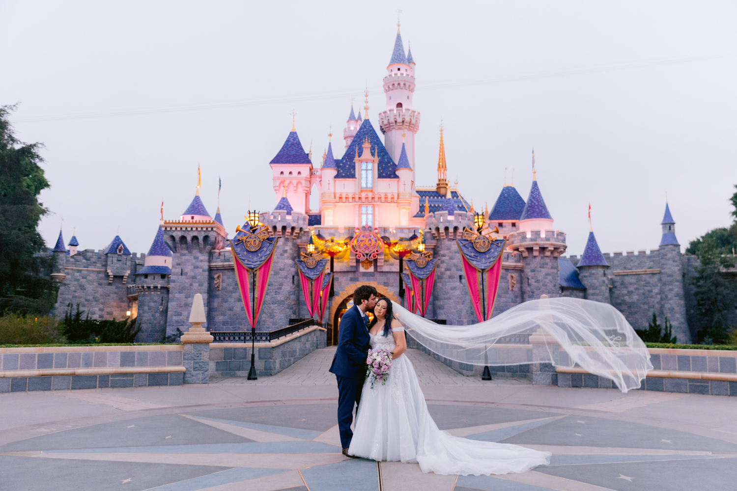 Couple posing in front of Sleeping Beauty Castle during sunrise portrait session at Disneyland